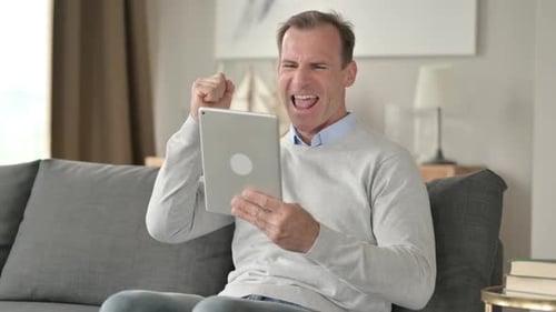Middle Aged Businessman Celebrating Success on Tablet at Home