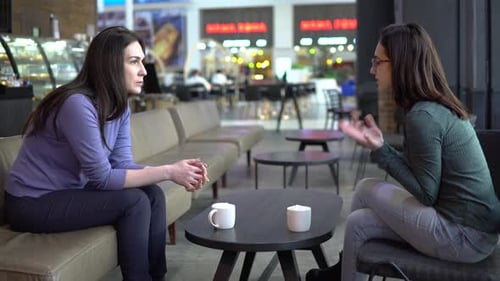 Junge Frauen sitzen in einem Café und unterhalten sich. Mama und Tochter sitzen aneinander und chatten