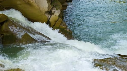 Mountain river with clear turquoise water falling down in cascades between wet boulders with