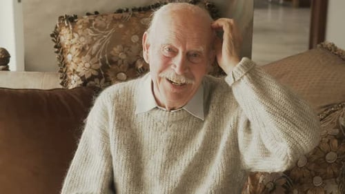Smiling Senior Man Talking on Couch Indoors