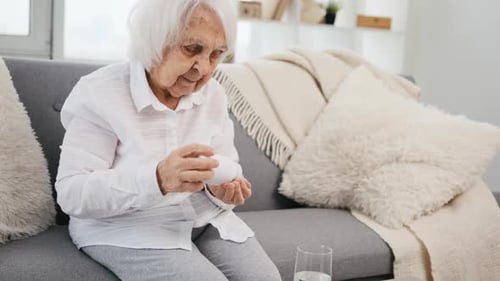 Senior Woman Taking Pills on Couch at Home