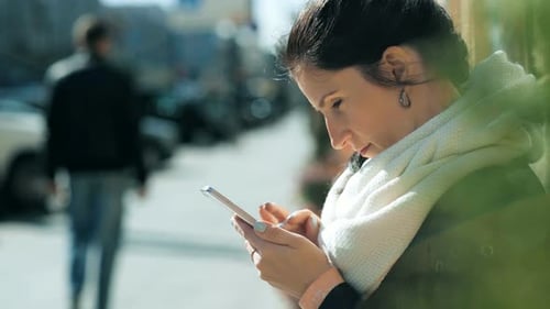 Beauty Fashion Young Women Texting with Smart Phone Sitting on a Bench in the Street