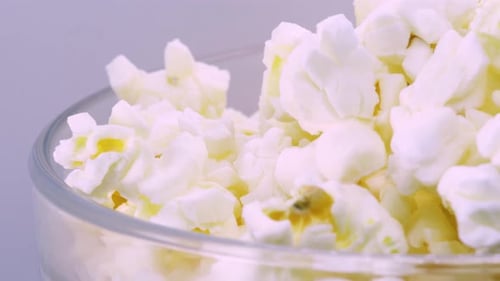 Popcorn doré et gras dans un bol en verre transparent, tournant. Prise de vue macro, vue rapprochée en 4k. Whi