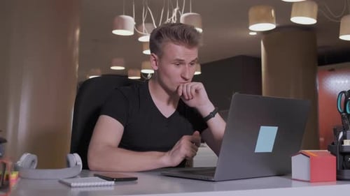 young business man sits at table with a laptop working in office. He gets great news
