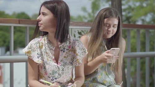 Young Women Writing and Listening to Music Outside
