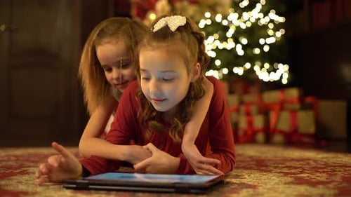 Festive Girls Enjoying Tablet by Christmas Tree