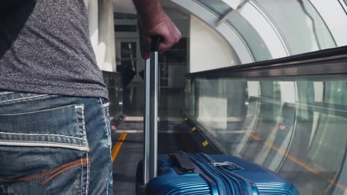 Young Caucasian Male Tourist Traveling on Vacation in Airport on Travelator Holding Luggage Wearing