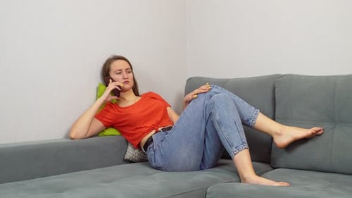 Woman Chatting on Smartphone Reclining on Gray Couch