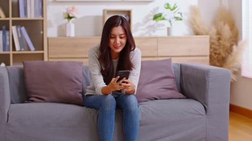 Woman Smiling Using Smartphone on Couch Indoors