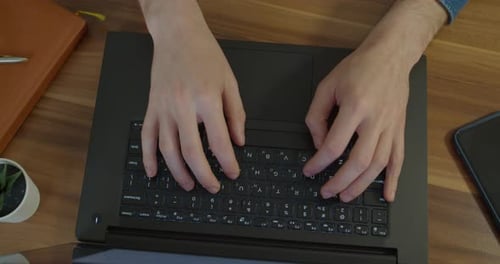 Man Hands Typing Text on Laptop Keyboard at Wooden Desk. Man Using Notebook for His Work at Home