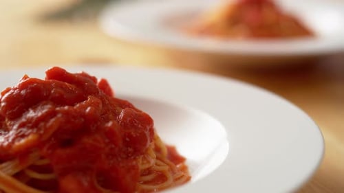 Camera follows putting fresh basil on tomato sauce pasta in plate. Slow Motion.