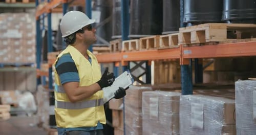 Logistics worker wearing a helmet working in a large warehouse checking inventory