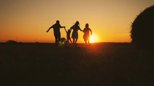 Family Runs Together Through Field at Sunset