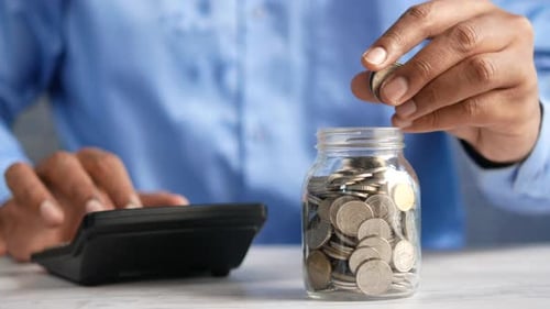 Close Up Hand Adding Coins to Savings Jar