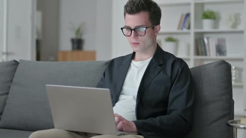 Man Sitting on Couch Celebrating Success with Laptop