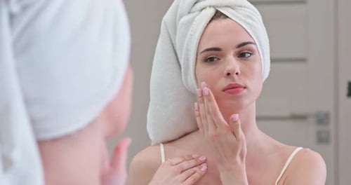 Woman Massaging Face and Neck in Bathroom Mirror