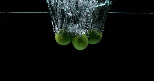 900452 Green Lemons, citrus aurantifolia, Fruits falling into Water against Black Background, Slow M
