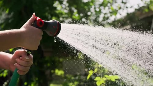 Nahaufnahme einer Gartenspritze bei einer Frau, die das Gartenbett von Hand bewässert