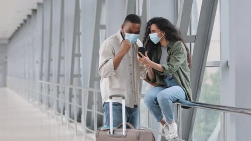 Multiracial Couple Hispanic Woman and African American Man Wearing Medical Masks Sitting in Airport