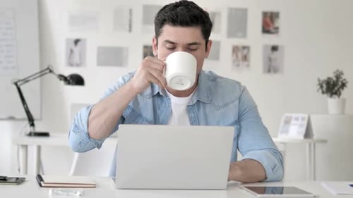 Lässiger junger Mann trinkt Kaffee während der Arbeit am Laptop