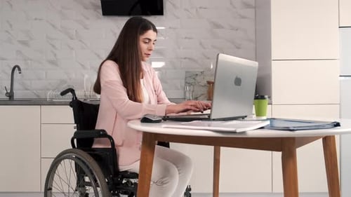 Young Disabled Woman in Wheelchair Working with Laptop and Tablet at Home