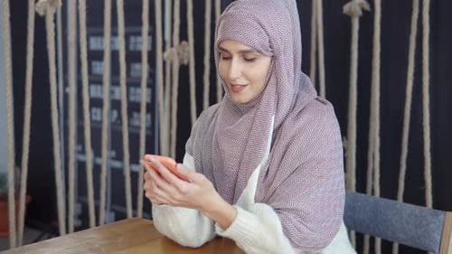 Woman in Headscarf Uses Smartphone at Table