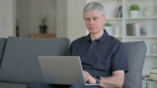 Mature Adult Using Laptop, Smiling on Couch