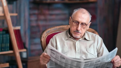 Pensive 70s Mature Grandfather Reading Paper Publication Newspaper Text Journal on Vintage Armchair