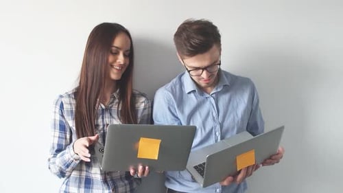 Glückliches Mix-Race-Paar hält Laptop in der Hand, während es steht und isoliert über grauer Wand feiert