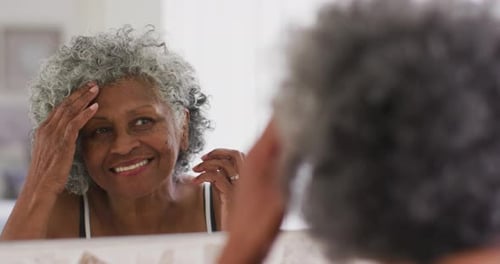 Senior african american woman touching her hair while looking in the mirror at home