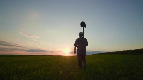 Silhouette eines männlichen Bauern, der bei Sonnenuntergang mit einer Schaufel auf dem Feld arbeitet, geht durch Ackerland