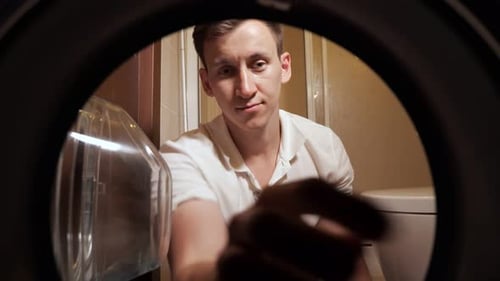 Young Man is Loading the Clothes to Washing Machine View From Inside