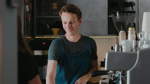 Handsome barista in a coffee shop making cappuccino coffee take away for a customer