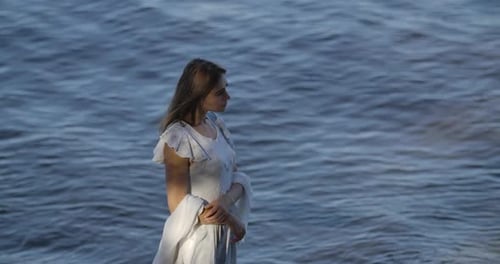 Vista superior de uma linda mulher caucasiana em vestido branco claro em pé no fundo das ondas do mar