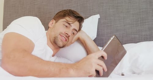 Happy Man Using Tablet Device in Bed