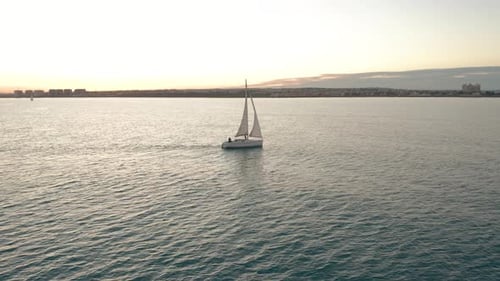 Luftaufnahme. Die Yacht segelt bei Sonnenuntergang auf dem Meer. Drohne fliegt mit Segeln um die Yacht herum.