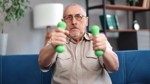 Senior Man Lifting Dumbbells on Couch Indoors