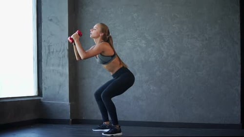 Woman Doing Squats with Dumbbells in Gym
