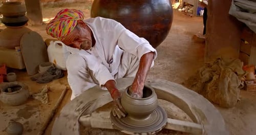 Potier indien au travail : lancer le volant du potier et façonner un récipient en céramique et des articles en argile : pot