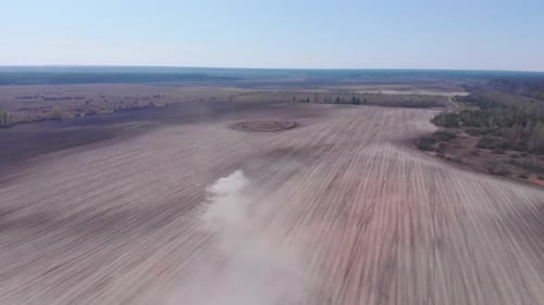 Combine plows land. Dust in field. Aerial view of tractor in field.