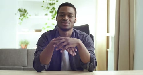 View From Webcam Afro American Young Friendly Guy Sits at Table at Home in Office Speaks Tells