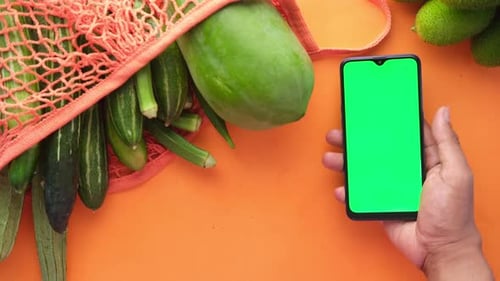 Top View of Man's Hand Holding Smart Phone with Fresh Vegetable on Table