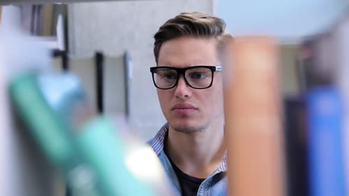 College Library. Male Student Searching For Book On Bookshelves