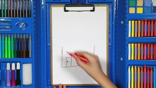 Die Hand des Mädchens zeichnet mithilfe verschiedener Marker die Zeichnung eines Kindes mit einem Haus
