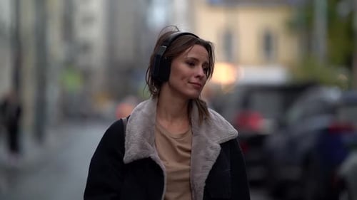 Calm and Relaxed Woman Is Strolling Alone in Town and Listening To Favorite Song in Headphones