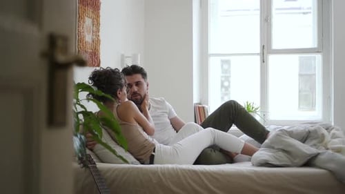 Junges amerikanisches Paar redet und umarmt sich, während es im weißen Schlafzimmer auf dem Bett liegt Spbd