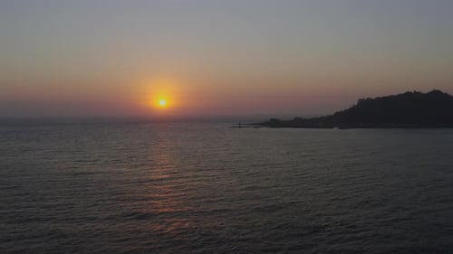 A seascape at sunset, where you can see the island, breakwater, and lighthouse