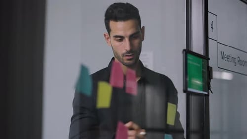 Man Planning Strategy Using Sticky Notes on Glass Wall