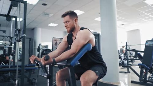 Side view of an athletic man during workout in a gym. Bodybuilder sitting in a modern simulator