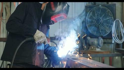 Welder welding metal parts in a workshop